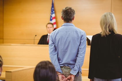 A handcuffed defendant and his attorney standing in a court of law.